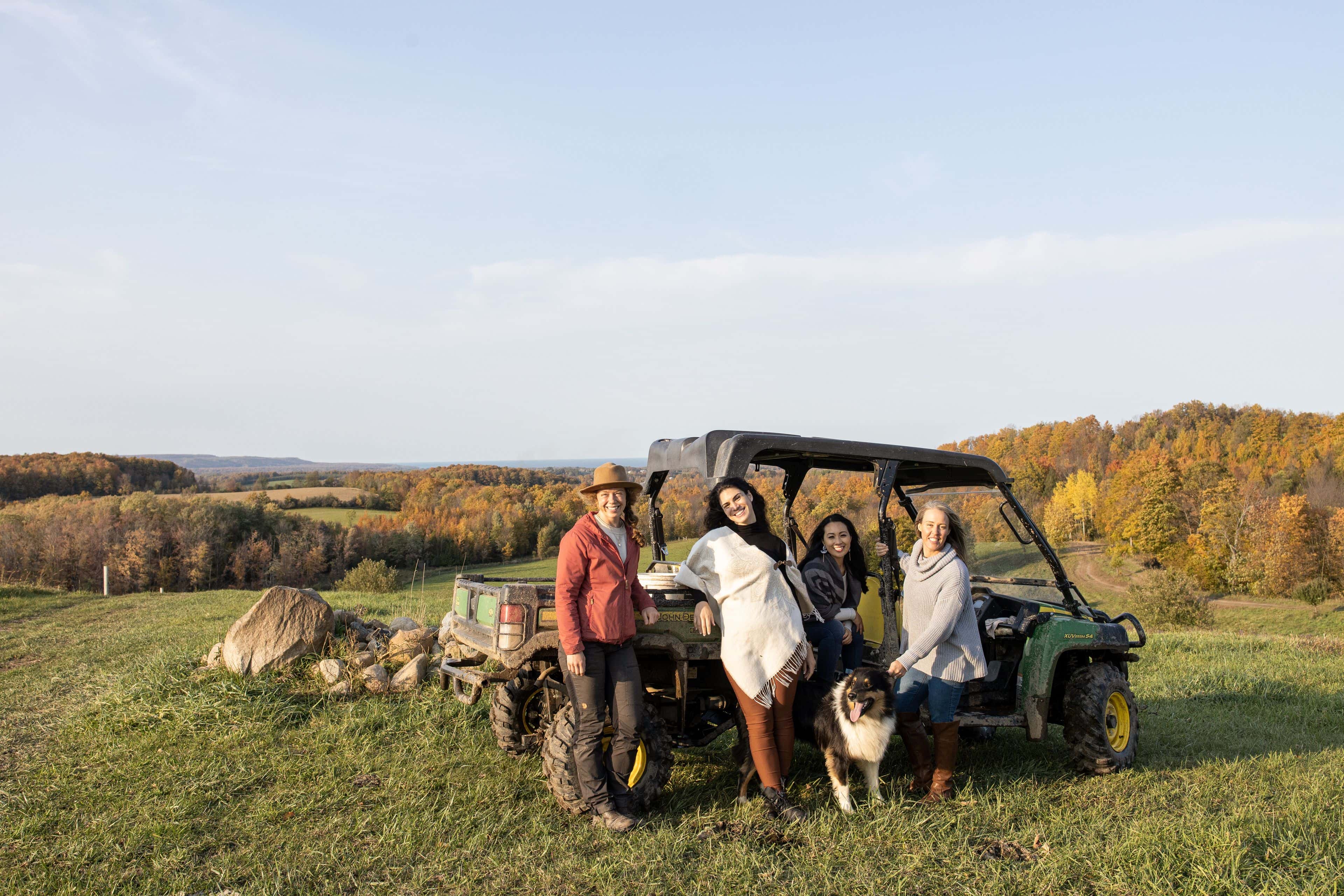 A group of girlfriends posing for a photo by the side-by-side tractor, surrounded by the vast acreage at Good Family Farms on a fall afternoon