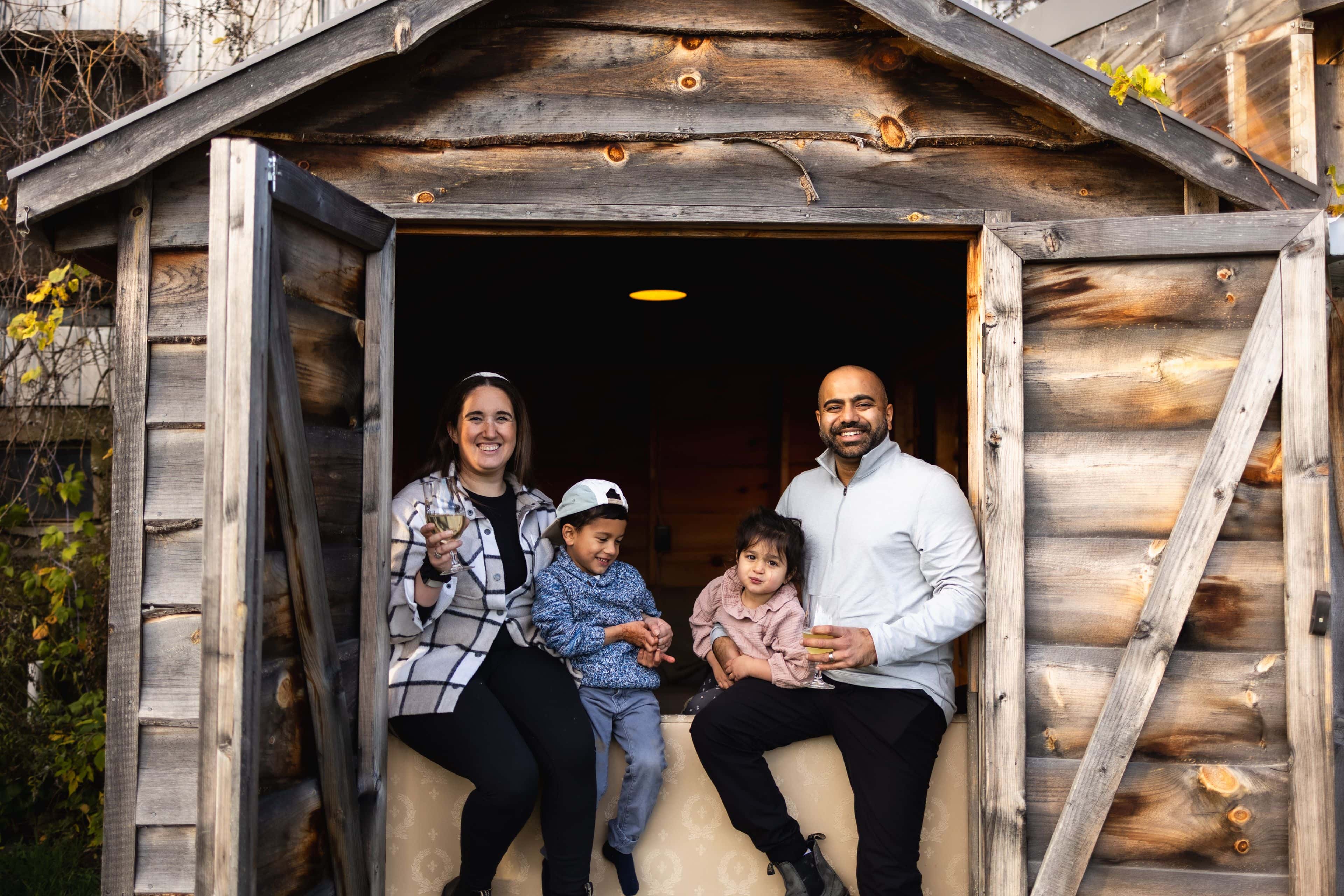 A family of four perched up in the window of a wooden shed for a group photo at Grey & Gold Cider in Clarksburg