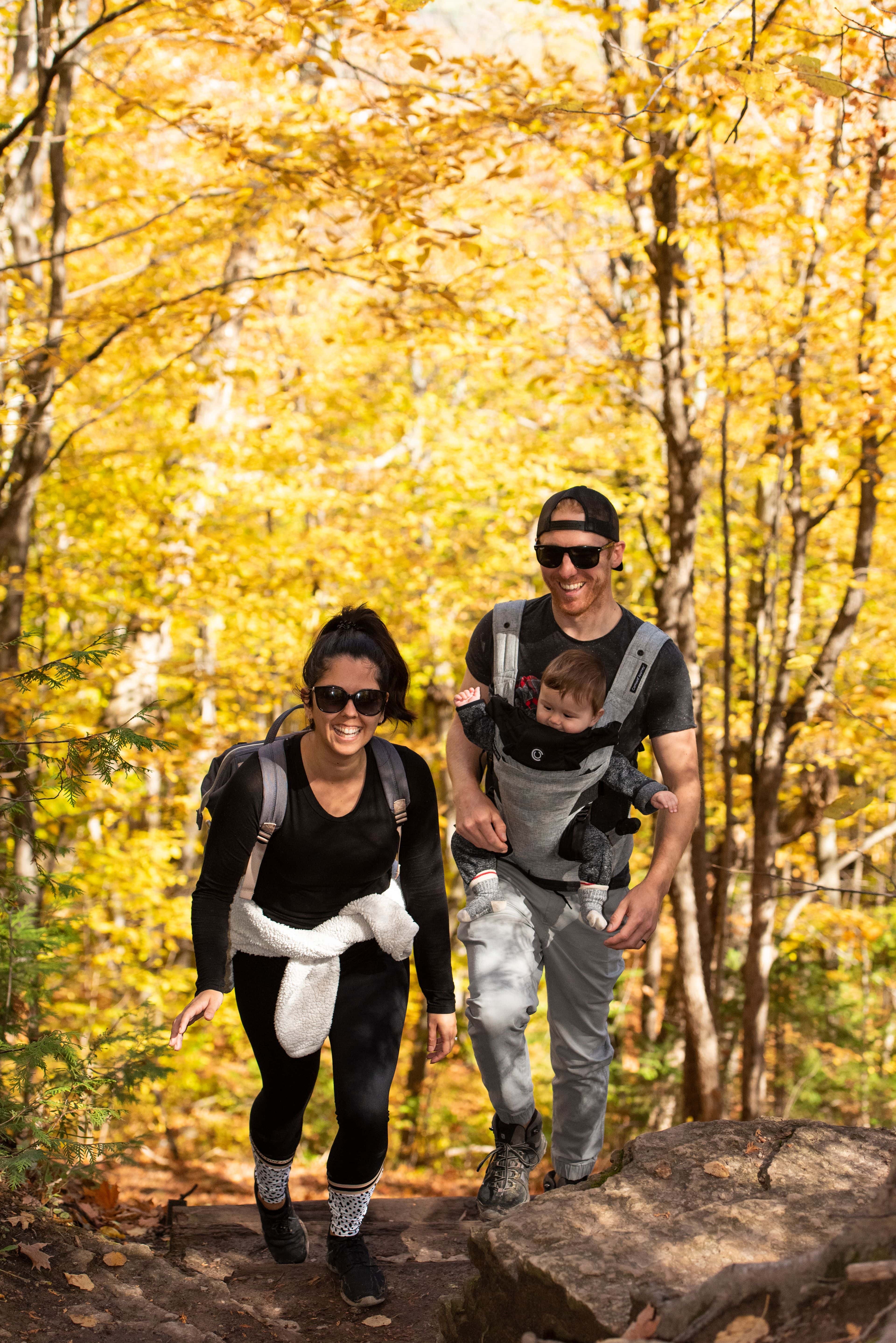 A young couple hiking up the Blue Mountain Trails with their baby in tow, surrounded by the amber leaves in the forest