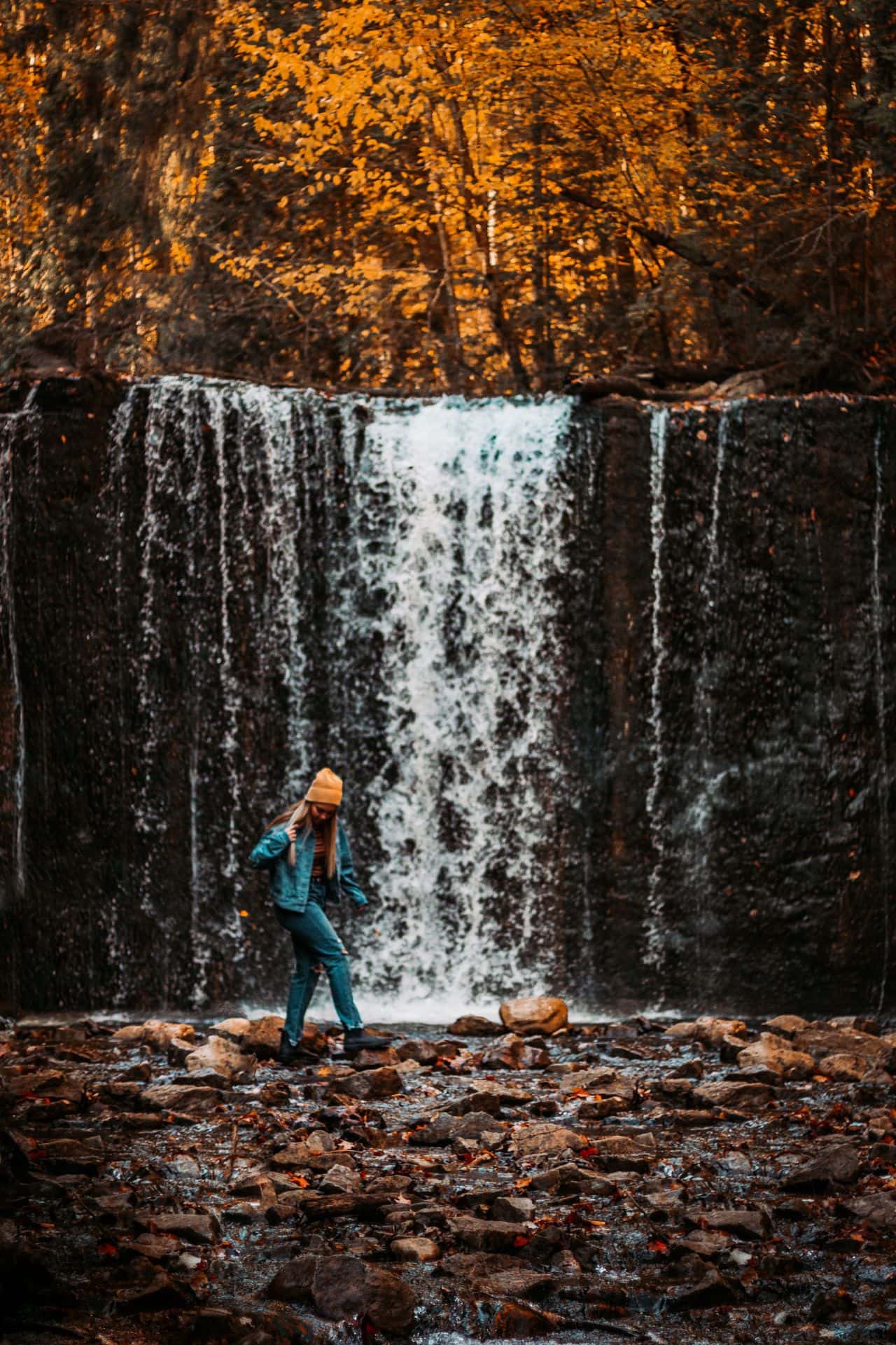 Woman walking across the rocks at the bed of a natural waterfall flowing along the trails on an autumn hike