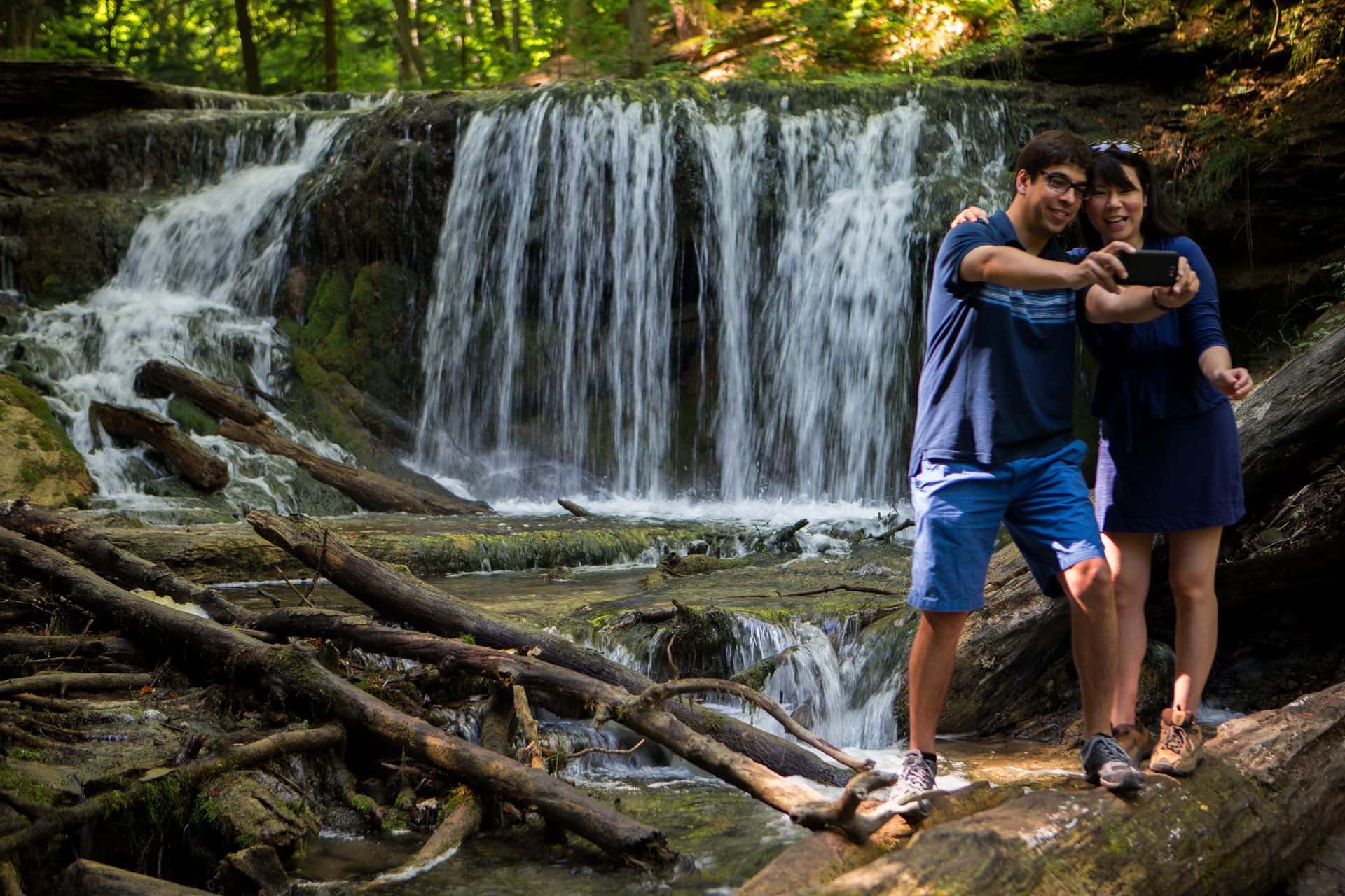 A couple taking a selfie in front of the natural waterfall along the hiking trail at Weavers Creek
