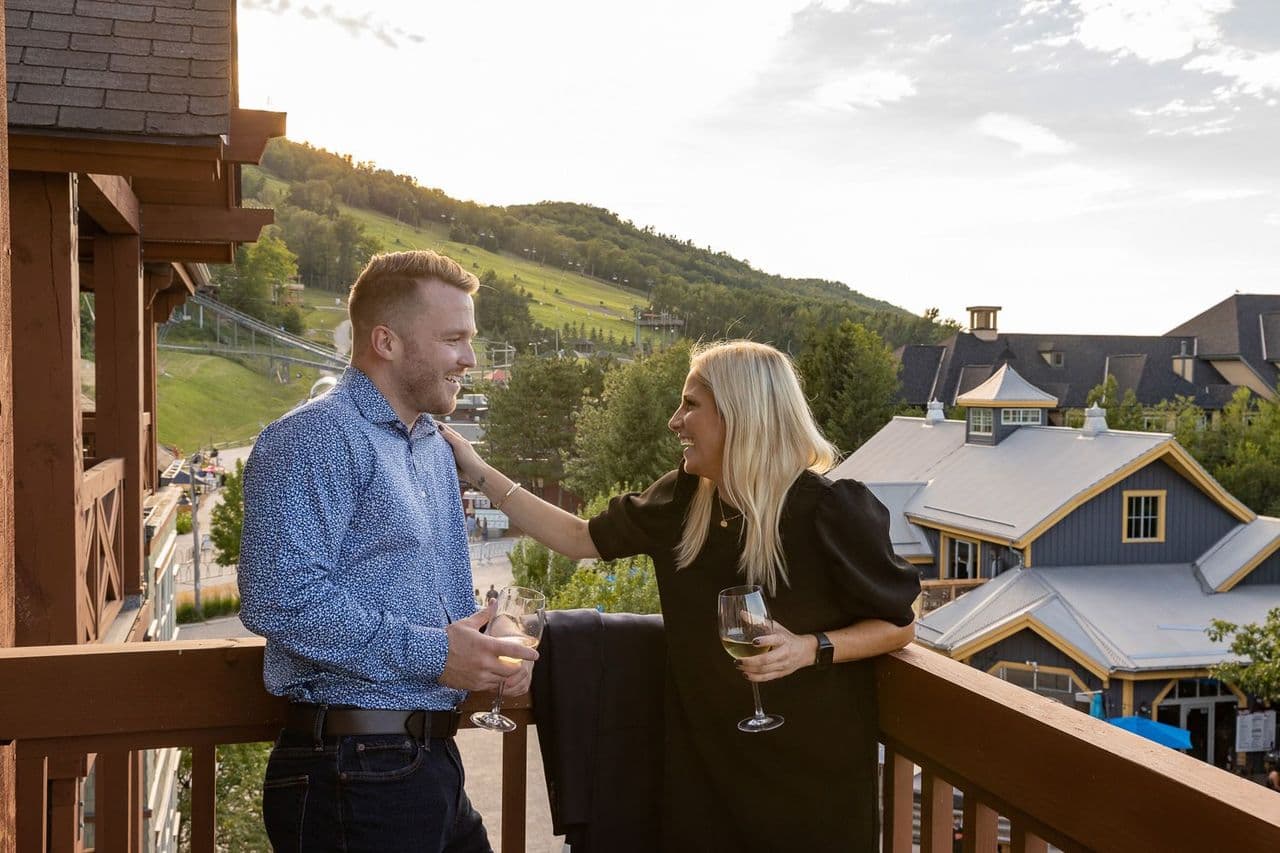 A couple stands on the patio in Blue Mountain Village drinking wine.