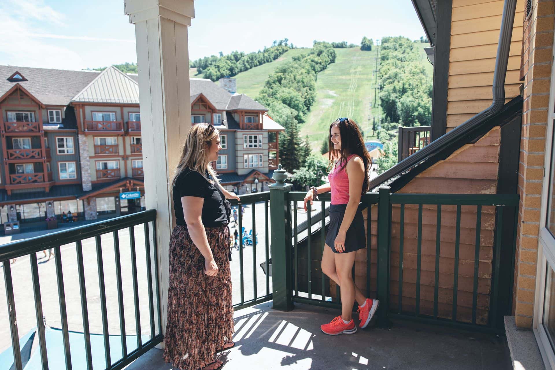 Two women chatting on the balcony of their Grand Georgian suite with views of Blue Mountain Resort and Village in the background