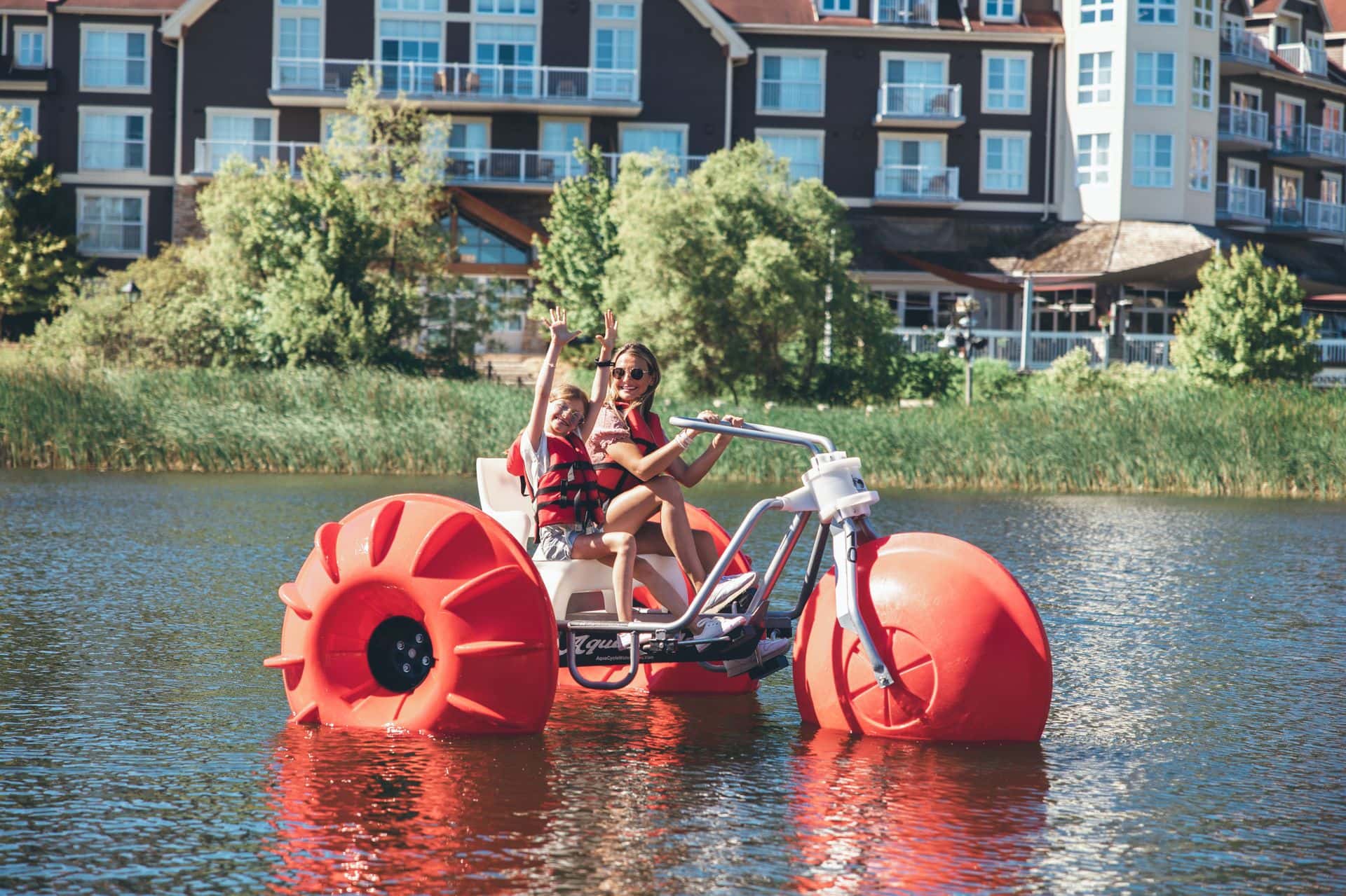 A mom and daughter smiling for the camera as they pedal along the Mill Pond on giant water trikes at Blue Mountain Resort.