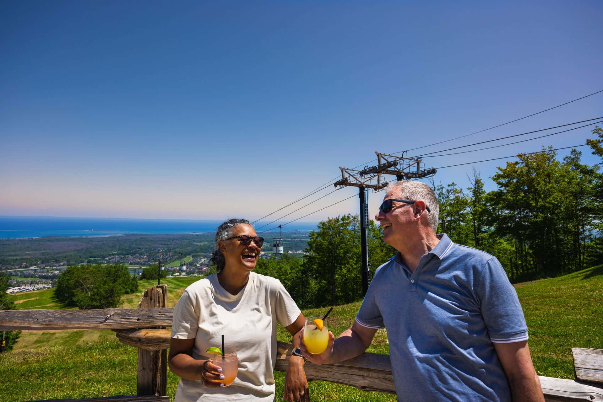 A couple enjoying cold beverages against the stunning view of Blue Mountain Village and Georgian Bay at Summitview Pavillion at Blue Mountain Resort