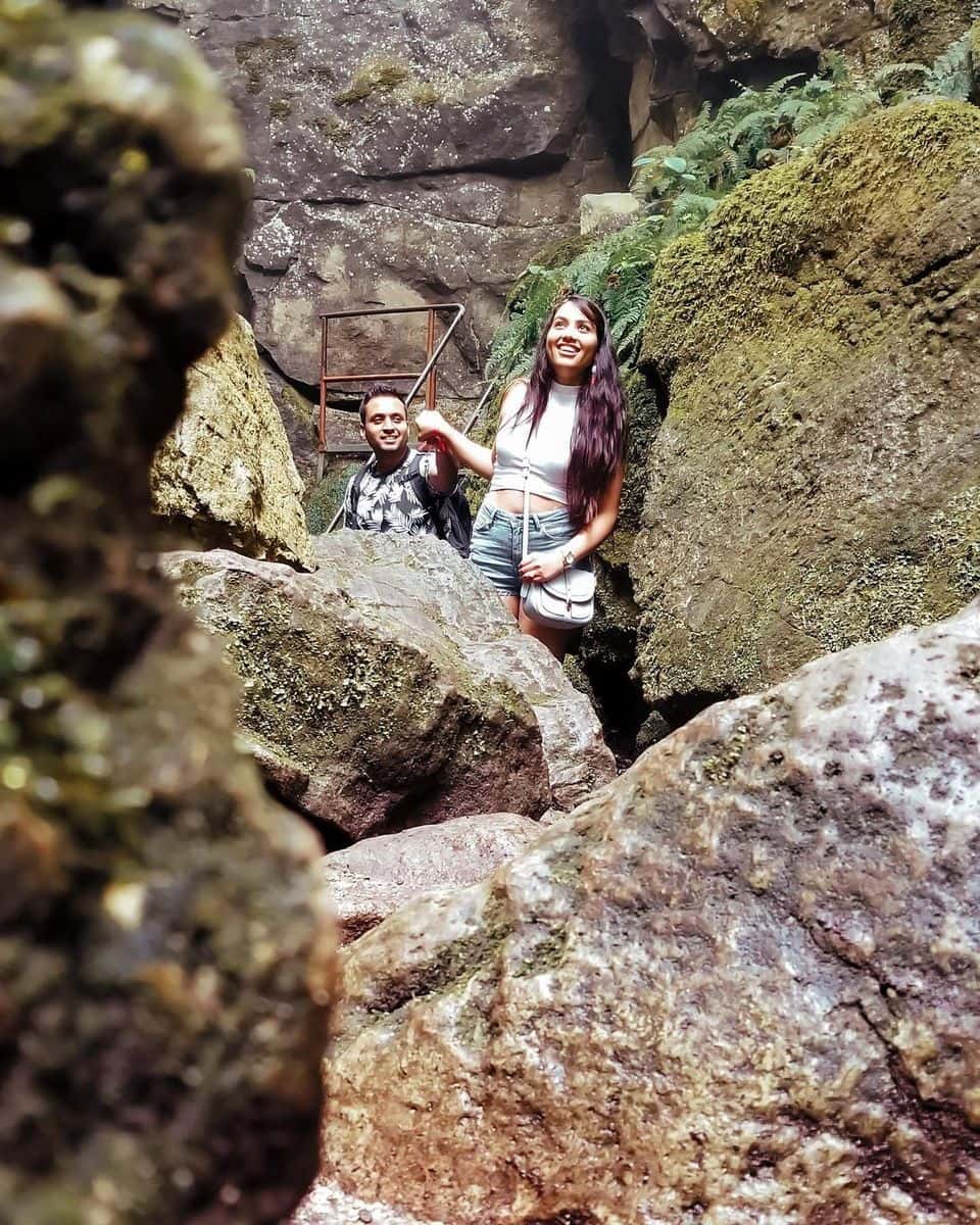 A couple peering around the giant rocks and boulders on a hike through the Scenic Caves/