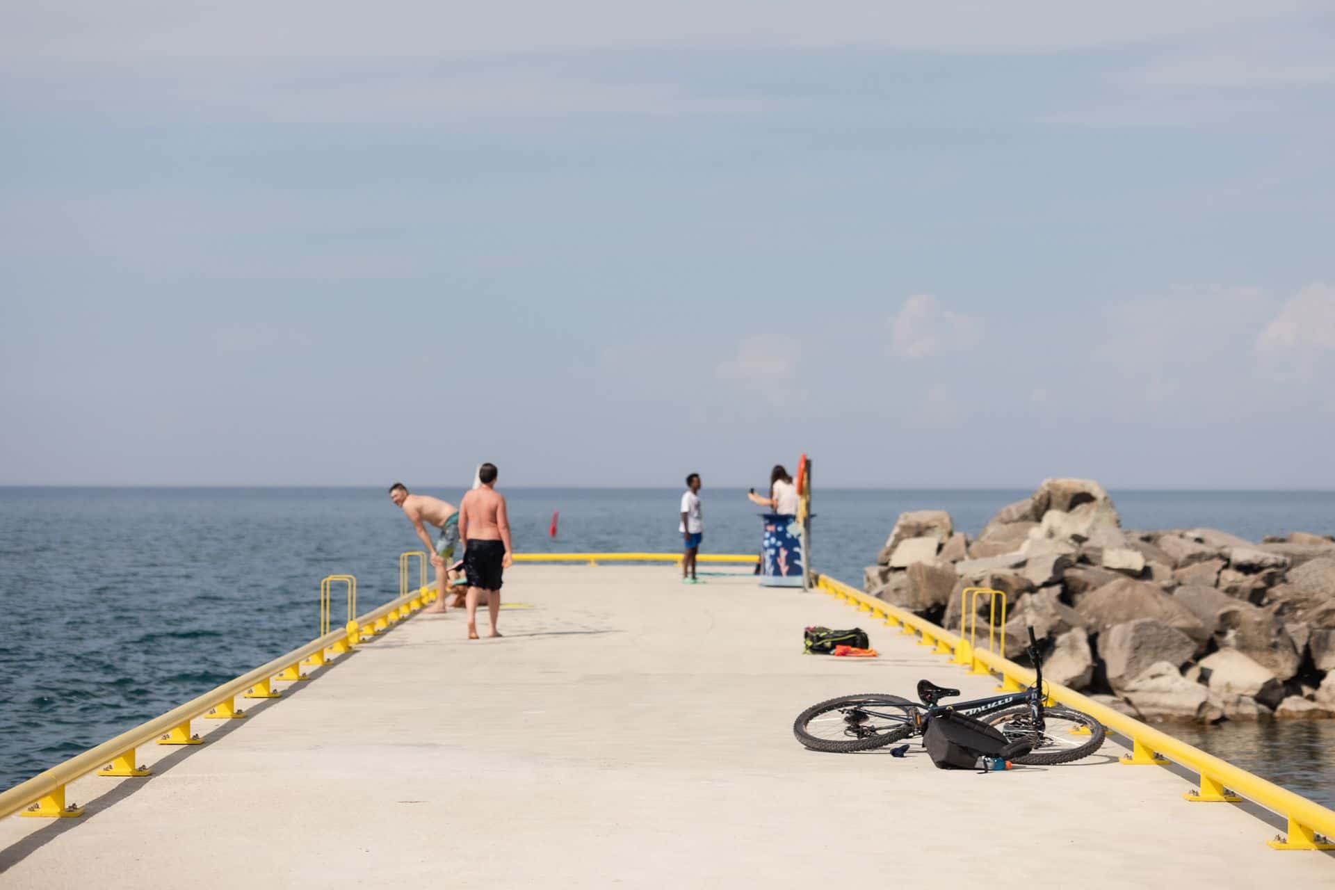 Some folks walking along the Thornbury pier while a couple other swimmers get ready to jump back in the water at Little River Park.