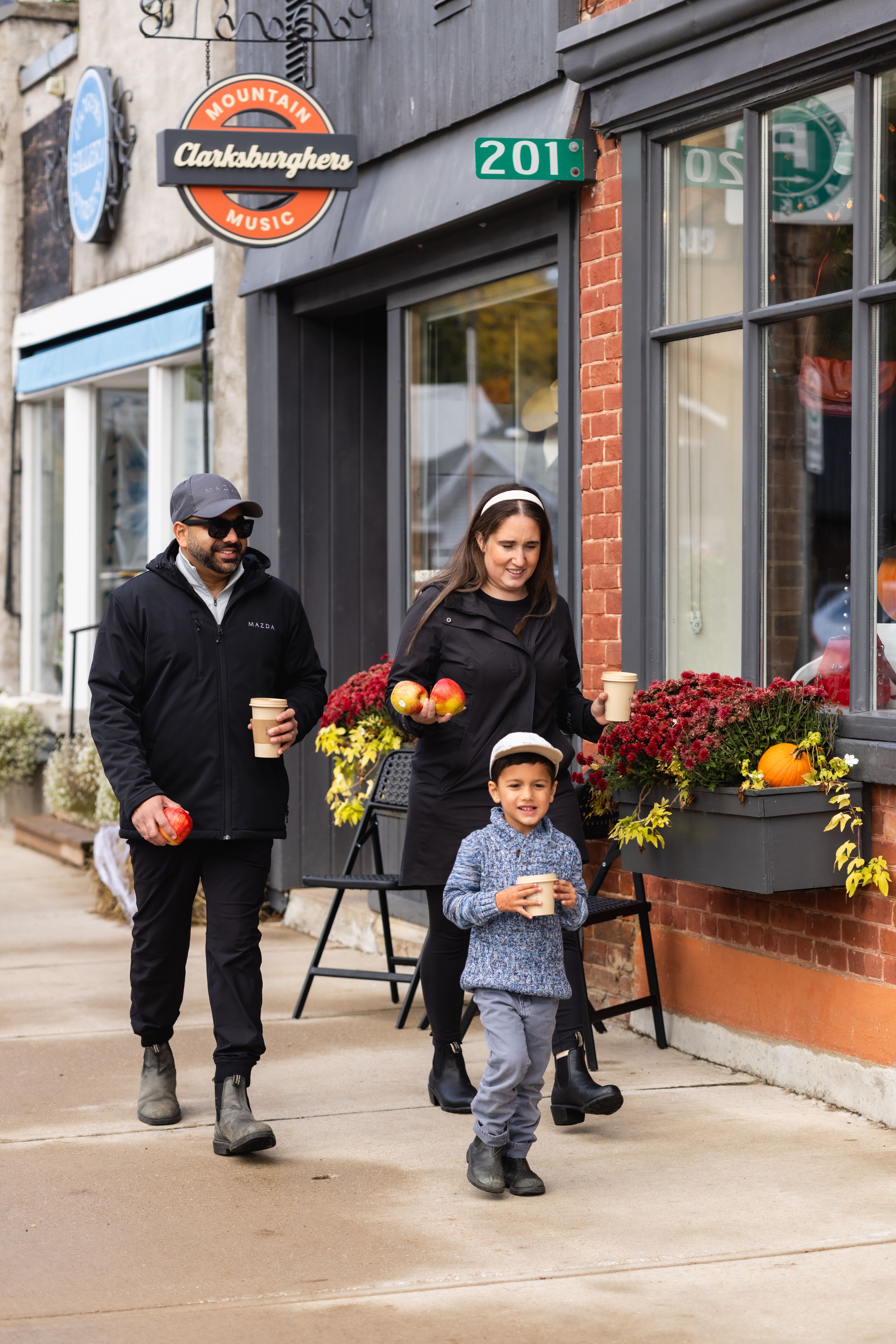 A family of three stroll down Marsh Street in Clarksburg with hot beverages in hand as they shop around on a Fall afternoon