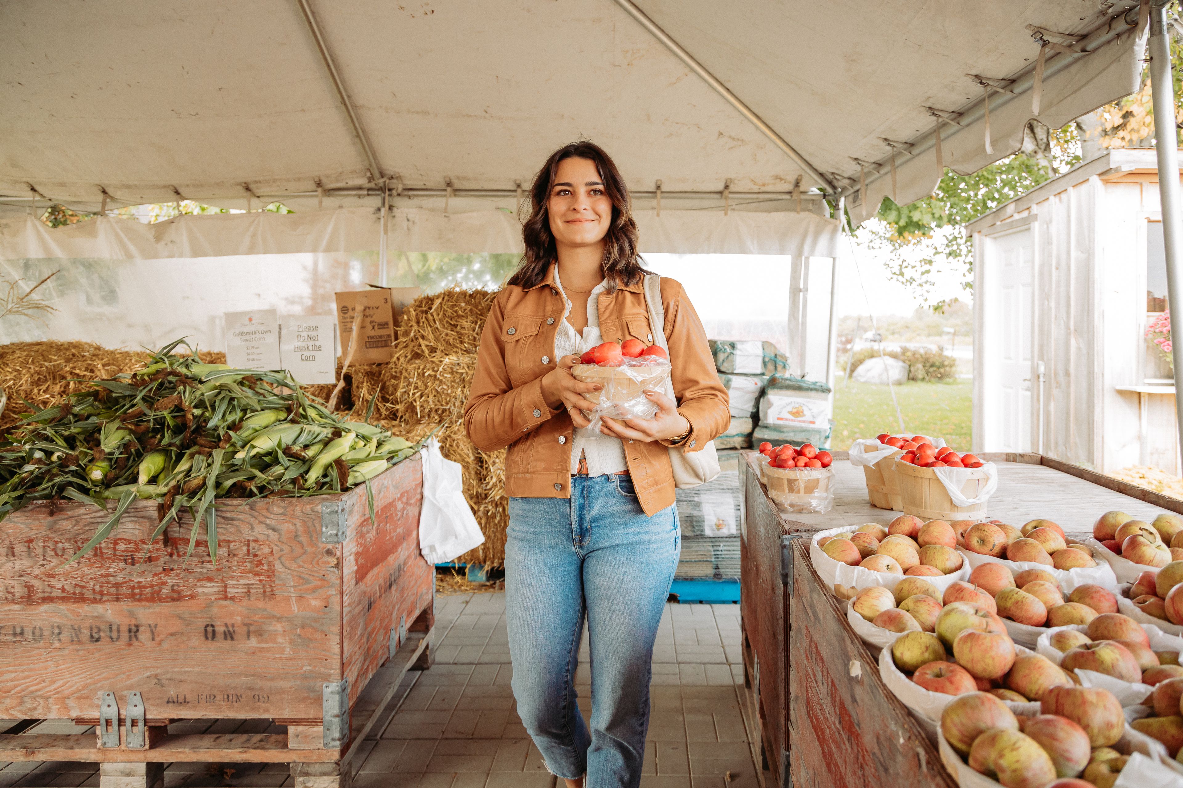 A woman walking through Gold Smith's Market with a basket of fresh local apples harvested in Fall at Blue.