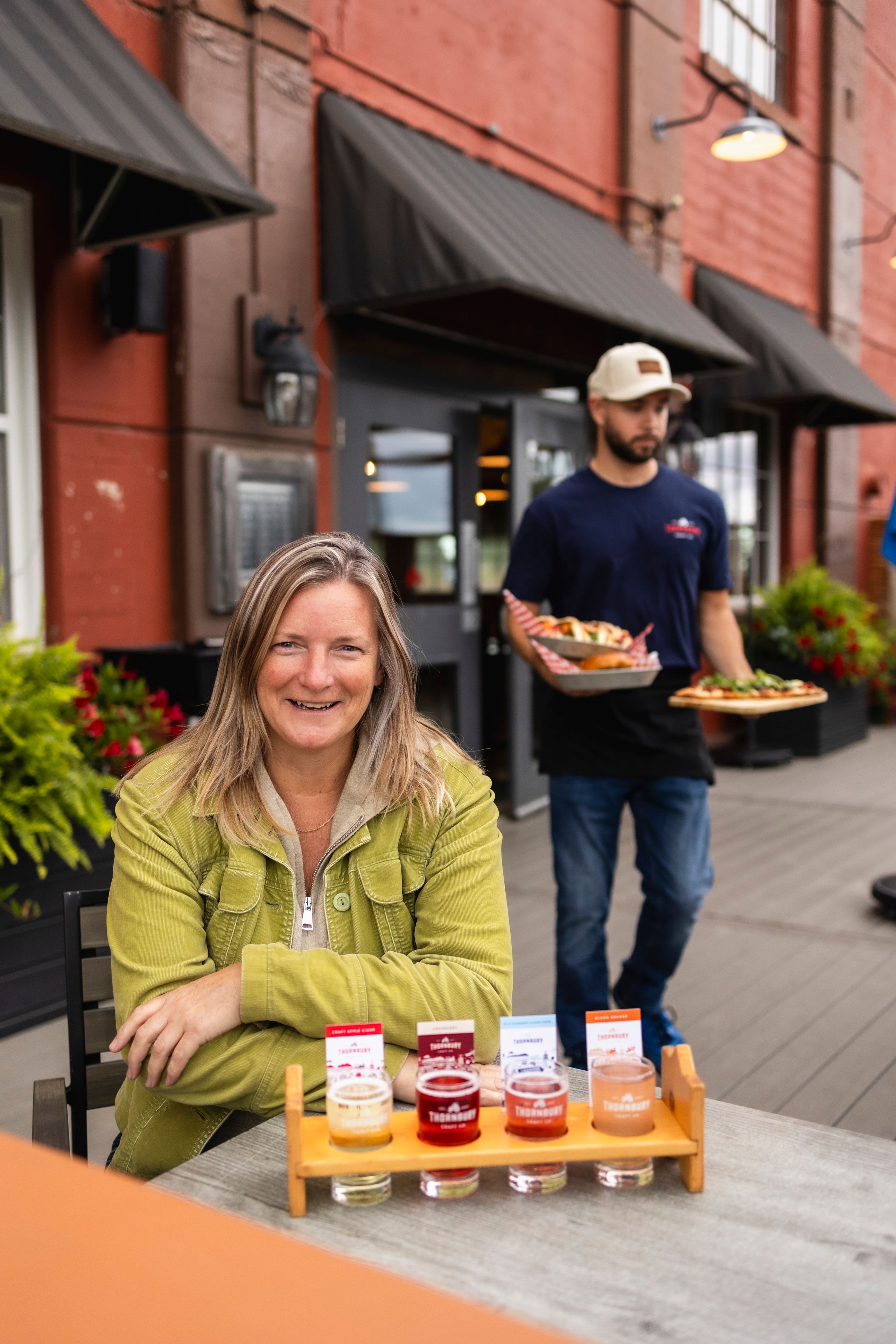 A woman smiles for the camera at Thornbury Cider before sipping on the cider flight in front of her.