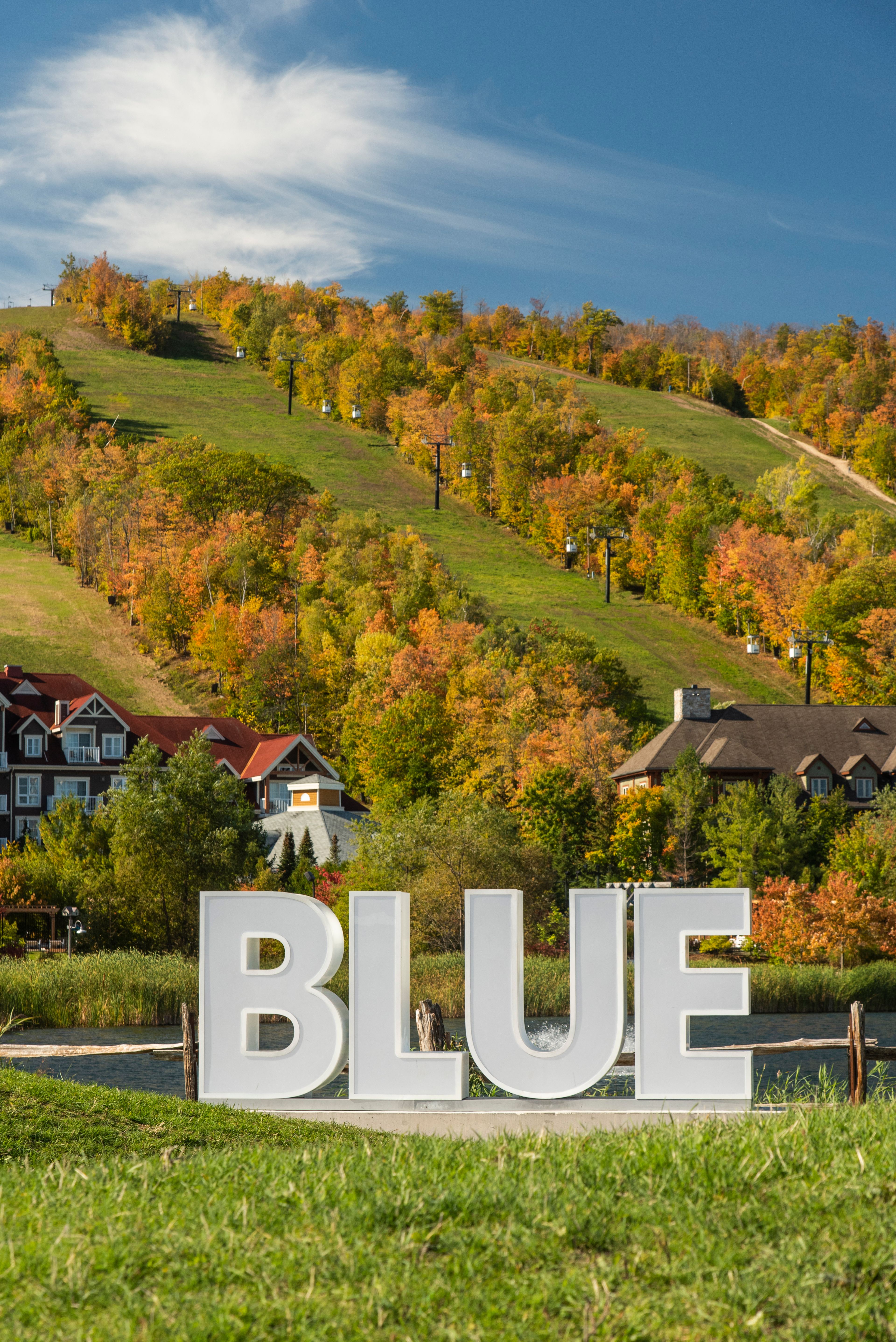 A shot of the BLUE sign set against the background of Blue Mountain Village and Resort in fall colours.