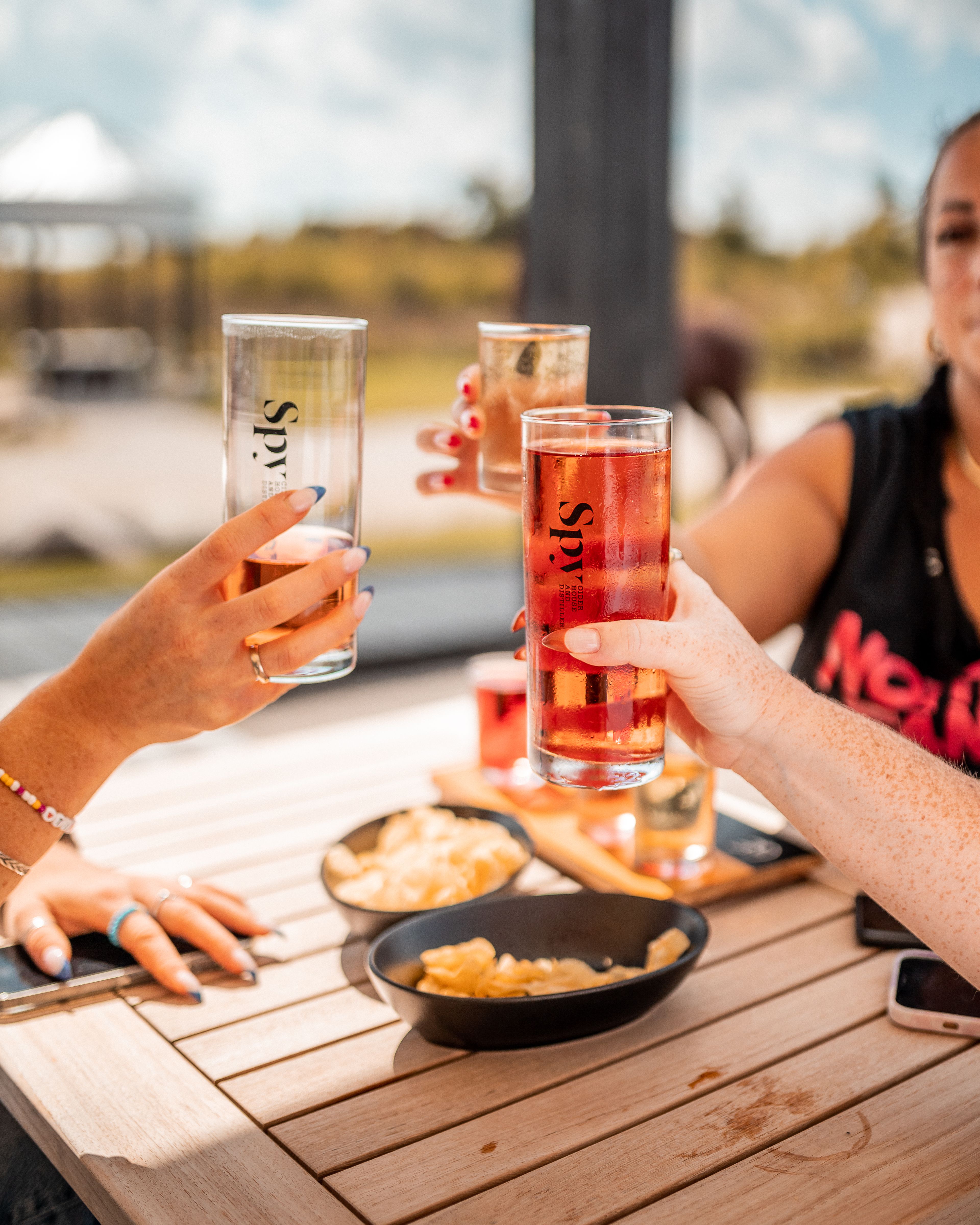 Friends clink together their glasses while enjoying local sips at Spy Cider House & Distillery on a sunny afternoon in Clarksburg.